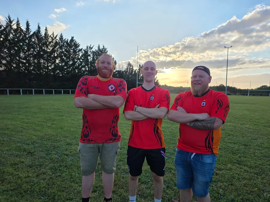 Trois joueurs en maillot du club, bras croisés, au coucher du soleil